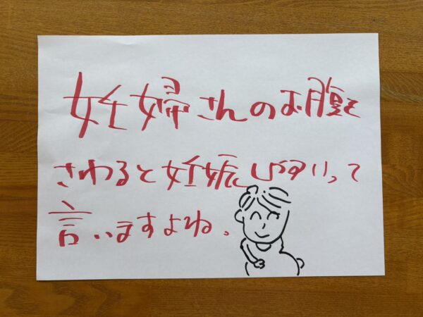 『妊婦さんのお腹を触ると妊娠しやすいといいますよね！』という場面を描いたイラスト。妊婦さんが優しくお腹に手を添え、そばで笑顔の女性がそのお腹にそっと触れている。春の柔らかな光と花に包まれた温かい雰囲気で、生命のつながりや希望を感じさせる構図。妊活、子宝祈願、チョコレート嚢胞、子宮内膜症、漢方ケアをテーマにした明るく優しいタッチのイラスト。