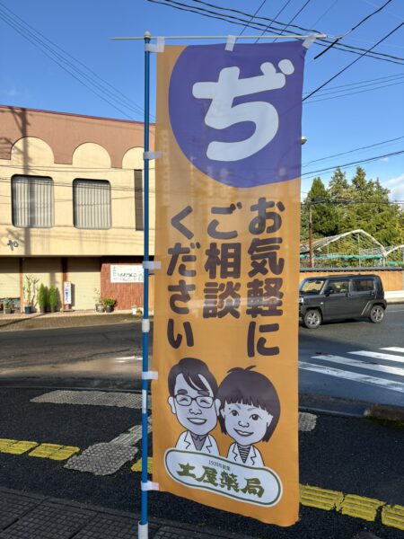 山形県東根市の土屋薬局前に掲げられたオレンジ色の「ぢ お気軽にご相談ください」ののぼり旗。痔の痛み・出血・腫れに漢方相談を行う薬局の外観。