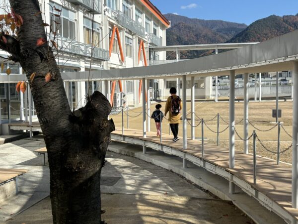 中庭を手をつないで歩く親子の後ろ姿。家族の温かさと安心感が伝わる微笑ましい瞬間を写した写真。