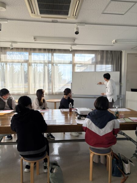 土屋薬局の土屋幸太郎が、リンクむらやまで開催した妊娠力アップセミナーで受講者に向けて講義している様子。スライドを示しながら妊活や漢方、体質改善について丁寧に説明している場面。