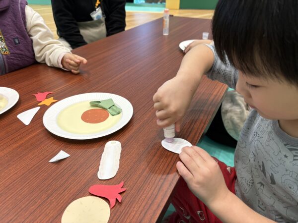 令和7年11月24日、長井市の『くるんと』で4歳の息子が工作教室で“おでん”の作品を作っている様子。先生方に温かく見守られ、楽しそうに制作する姿が伝わる写真。