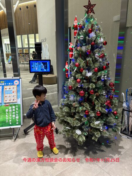 4歳の息子(僕ちゃん社長)が、長井市の『くるんと』の店内でクリスマスツリーの横に立ち、にっこり笑顔でピースサインをしている写真。冬の訪れを感じる温かい家族のワンシーン。
