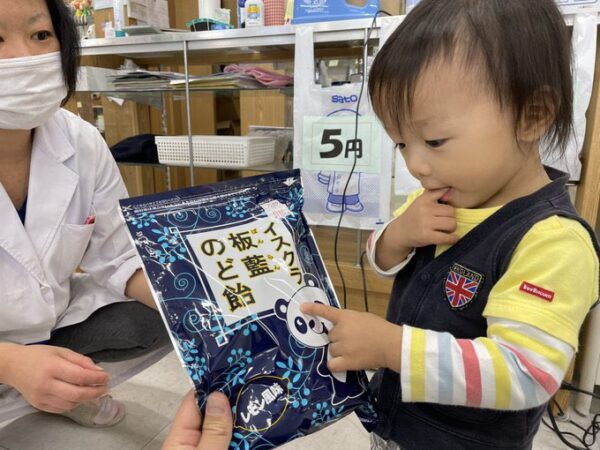 令和5年のコロナ感染症対策が大変だった時期、2歳頃の子どもが板藍のど飴のパンダデザインを指さしている写真。母親と一緒に過ごす温かい家庭の様子。