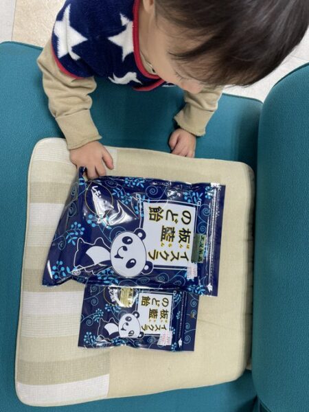 幼い息子が板藍のど飴のパンダデザインを指差し、嬉しそうに見ている様子。冬の感染症対策として板藍根入りのど飴に興味を示した瞬間。