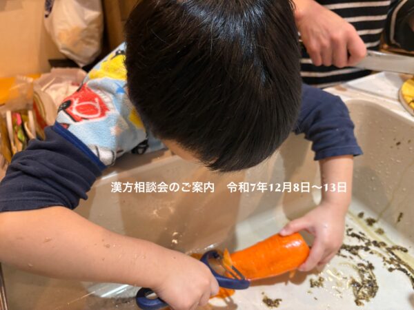 小さな息子がキッチンで人参の皮むきをしている様子。小さな手で一生懸命皮をむく姿が、家族の温かさや養生の心を感じさせるシーン。