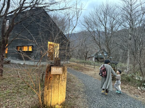 冬の川崎町、山沿いにある一軒の珈琲店へ、妻と息子が寄り添いながら歩いていく後ろ姿。周囲の林は枯れ木に包まれている。