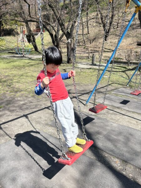 若木山公園でブランコに立ち乗りして遊ぶ幼稚園児の息子|春の昼休みの風景
