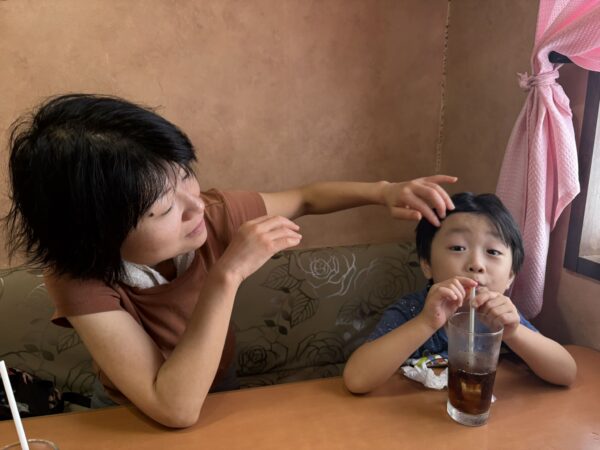東根市の洋食店「パパアンドママ」で家族ランチを楽しむ5歳の息子。コーラを飲みながら、母親が優しく髪をなでる笑顔の一枚。