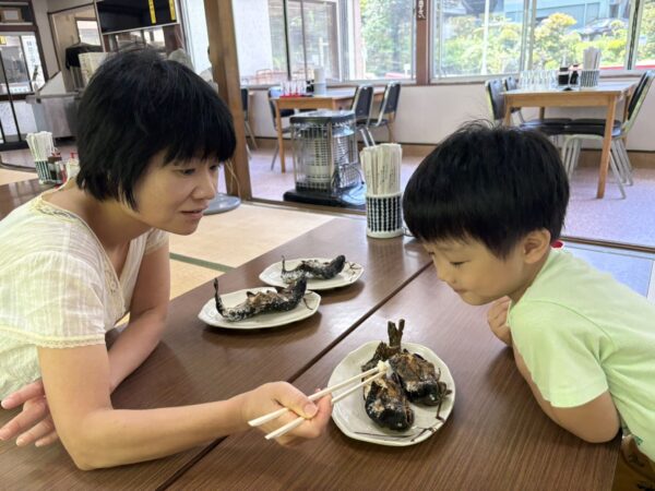ニジマスの塩焼きを妻から食べさせてもらう息子