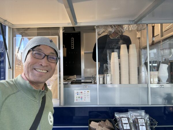 BLUE COFFEEの移動販売の前で喜ぶ土屋幸太郎です。