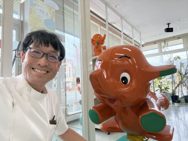 山形県東根市の土屋薬局店頭に立つ薬剤師・土屋幸太郎とサトちゃんムーバー