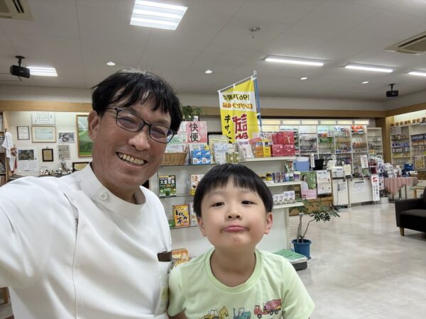 シルバーウィーク初日の営業終了後、土屋薬局の店内で5歳の息子と写る薬剤師の土屋幸太郎