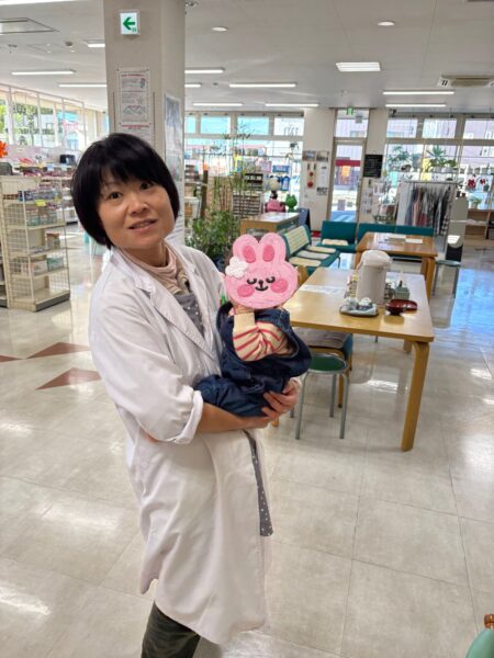 ご来店くださったお客様の赤ちゃんを抱っこする土屋薬局の妻